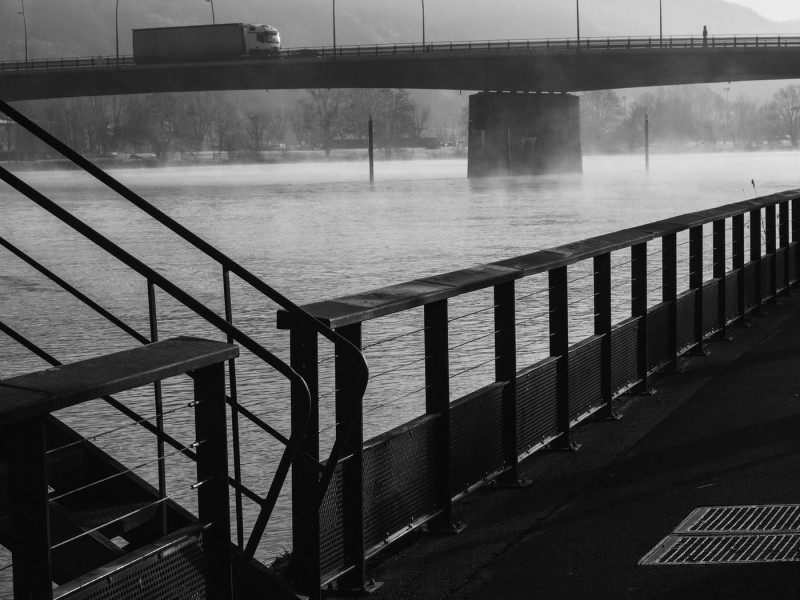 The River Seine at Vernon, Normandy, France. | Monochrome image of a misty river with a bridge in the background, viewed from behind a metal railing.