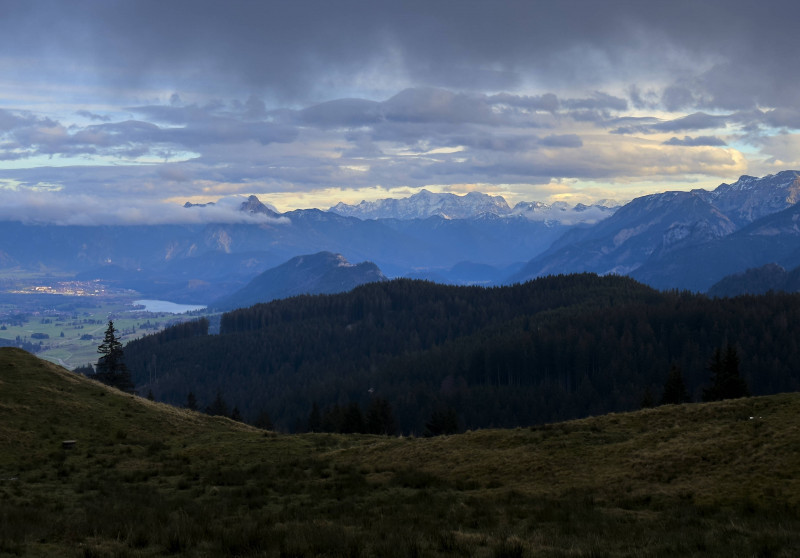 Hiker walking up to Edelsberg peak with Sportheim Böck mountain hut and a view on Weissensee an Neuschwanstein castle in