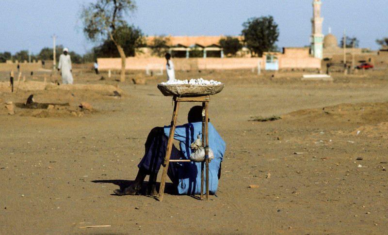 OMDURMAN, SUDAN - MAR 17, 1984: mansells sweets and protects himself from the midday heat by sitting in the shadow of the basket in Omdurman, Sudan.