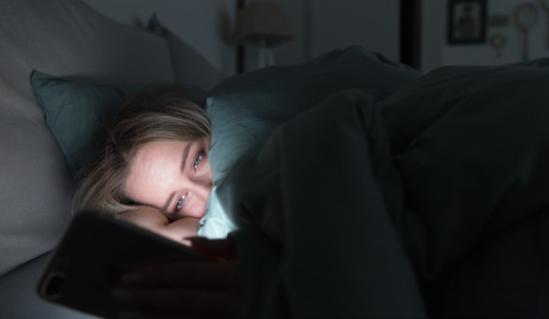 femeie in pat, care nu poate dormi si sta pe telefon