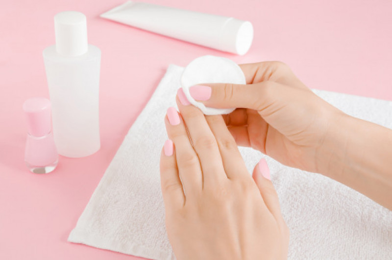 Woman's hand removing pink nail polish with white cotton pad on towel. Closeup.