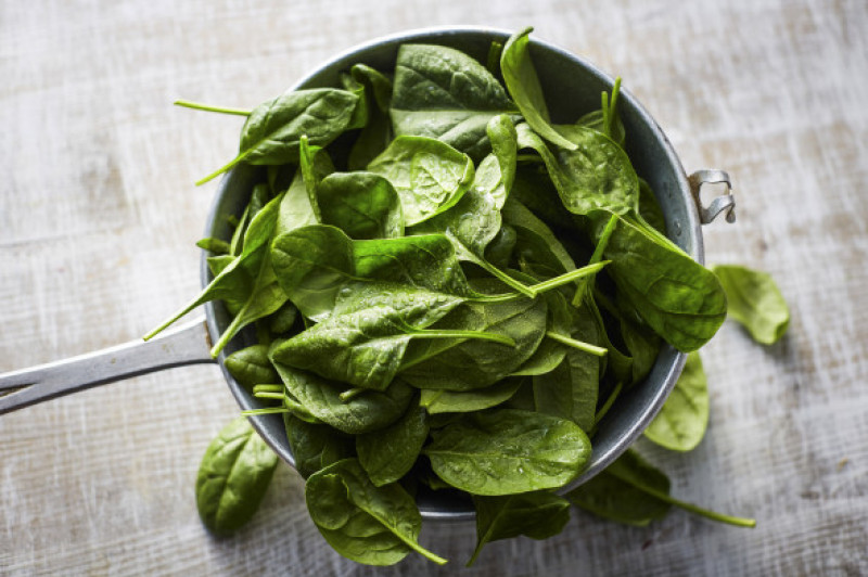 Fresh spinach leaves in colander on wood