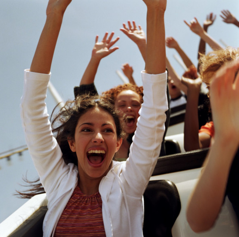 Teenagers (14-17) riding   rollercoaster, hands raised in air