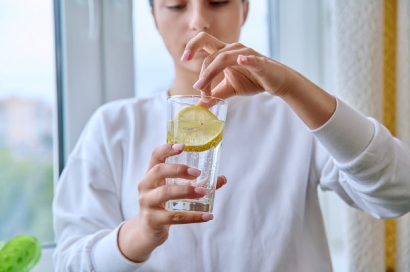 Close-up of glass of water with lemon in hands of young female