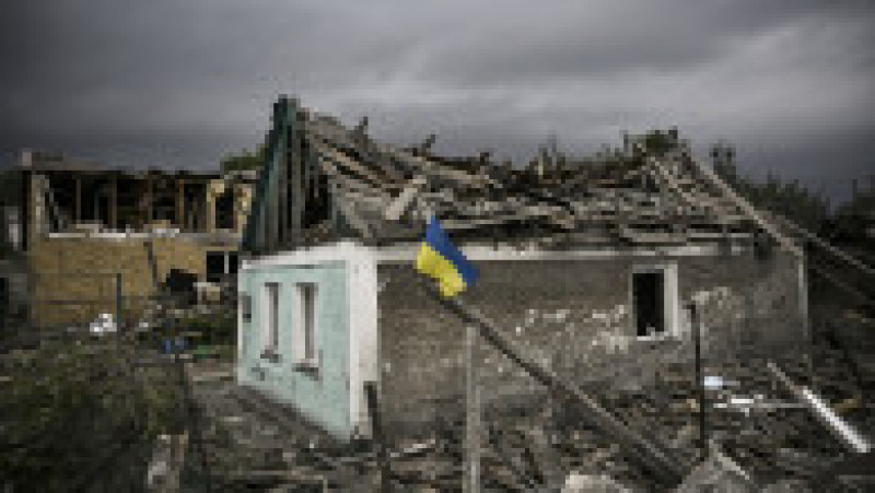 Un steag ucrainean flutură în fața unei case distruse de bombardamentele din orașul Dobropillia. Foto: Profimedia Images | Poza 2 din 10