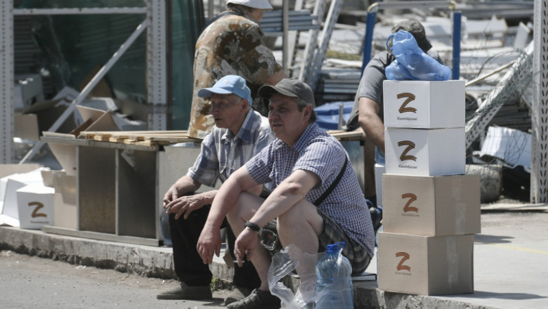 Oameni din Mariupol stau lângă cutii cu ajutoare umanitare pe care este scrisă litera Z, simbolul invaziei în Ucraina. Foto: Profimedia