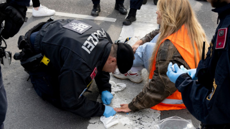 Polițiști austrieci în timp ce încerca să o elibereze pe o activistă lipită cu adeziv de asfalt. Foto: Profimedia Images