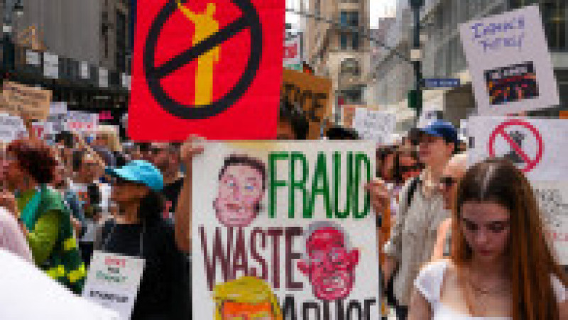 Manifestanți anti-Trump în New York, cu pancarte critice la adresa președintelui și a unor figuri publice. Pe fundal, se pot observa bannere cu mesaje de tip „Fraudă, risipă, abuz” și „Democrația cere respectarea procesului legal”.Foto: Profimedia | Poza 3 din 9