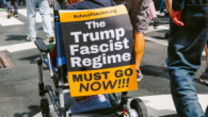 O persoană aflată în scaun cu rotile afișează un mesaj dur împotriva lui Donald Trump în timpul manifestației din New York: „Regimul fascist al lui Trump trebuie să plece acum”. Foto: Profimedia | Poza 1 din 9