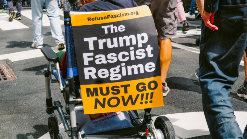 O persoană aflată în scaun cu rotile afișează un mesaj dur împotriva lui Donald Trump în timpul manifestației din New York: „Regimul fascist al lui Trump trebuie să plece acum”. Foto: Profimedia