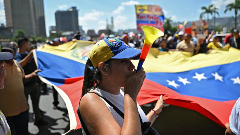 Venezuela: Forţele de ordine folosesc gaze lacrimogene împotriva protestatarilor îndreptaţi spre Miraflores 2 Oponenţi ai preşedintei interimare Delcy Rodriguez protestează la Caracas, pe 9 aprilie 2026, cerând majorarea salariilor şi pensiilor, cu un uriaş drapel venezuelean. Foto: Profimedia Images