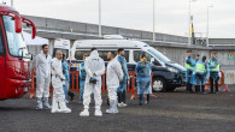 Persoane îmbrăcate în salopete de protecție așteaptă în port în timp ce nava de croazieră MV Hondius ancorează în apropierea portului Granadilla, pe 10 mai 2026, în Granadilla de Abona, Tenerife, Insulele Canare (Spania). Foto: Profimedia | Poza 6 din 10