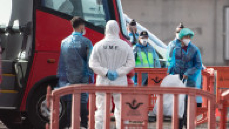 Un pasager (dreapta) poartă un costum de protecție și o mască în timp ce urcă într-un autobuz militar, în timp ce pasagerii și echipajul sunt evacuați de pe nava de croazieră MV Hondius, sub pavilion olandez și afectată de un focar de hantavirus, în portul industrial Granadilla de Abona de pe insula Tenerife, din Insulele Canare, Spania, pe 10 mai, 2026. Foto: Profimedia | Poza 1 din 10