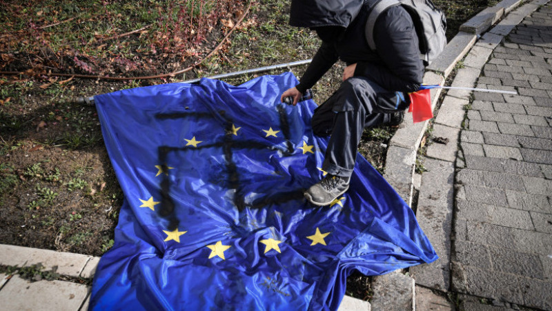 Un protestatar desenează o svastică pe un steag al UE în timp ce sute de oameni asaltează intrarea Parlamentului României. Foto: Profimedia Images/ Daniel Mihailescu
