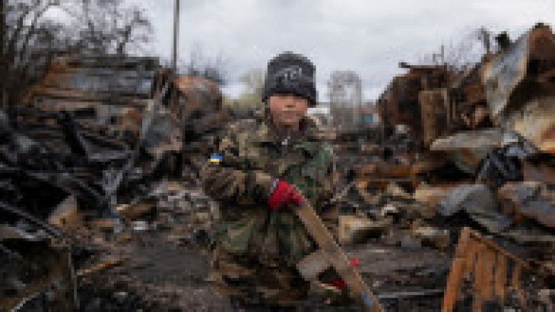 Yehor, un copil ucrainean în vârstă de 7 ani, ține în mână o pușcă de jucărie din lemn lângă vehiculele militare rusești distruse în apropiere de Chernihiv. Foto: Profimedia Images | Poza 9 din 11