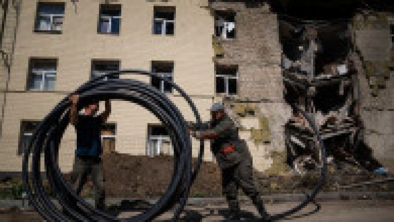 Muncitorii municipali pregătesc un nou tub pentru a restabili alimentarea cu apă în fața clădirii avariate de un atac rusesc la Bahmut, oraș din regiunea Donețk. Foto: Profimedia Images | Poza 11 din 13