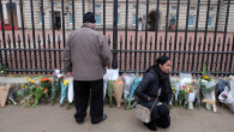 O femeie a îngenunchiat lângă buchetele de flori care au fost lăsate lângă gardul Palatului Buckingham Foto: Mihai Feflea | Poza 4 din 10