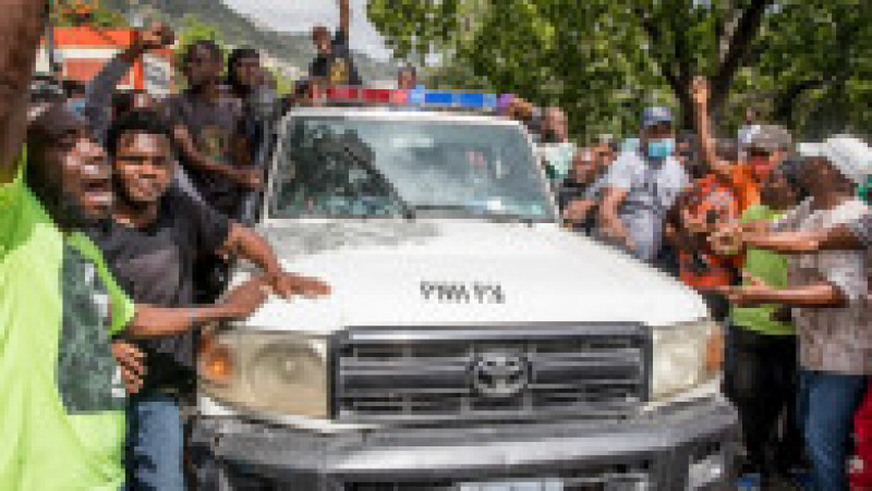 Cetățenii din Haiti se bucură în timp ce o mașină de poliție trece pe lângă secția Petionville din capitala Port au Prince, unde suspecții în cazul uciderii președintelui Jovenel Moise sunt reținuți. Sursa foto: Profimedia Images | Poza 6 din 38