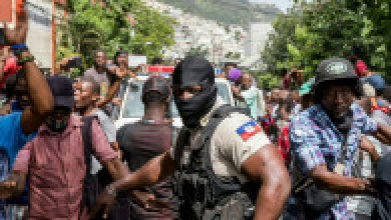 Cetățenii din Haiti se bucură în timp ce o mașină de poliție trece pe lângă secția Petionville din capitala Port au Prince, unde suspecții în cazul uciderii președintelui Jovenel Moise sunt reținuți. Sursa foto: Profimedia Images | Poza 25 din 26