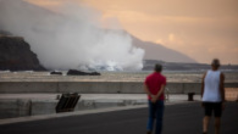 Doi oameni privesc la apus cum lava vulcanului Cumbre Vieja ajunge în apa Oceanului Atlantic. Sursă foto: Profimedia Images | Poza 7 din 8