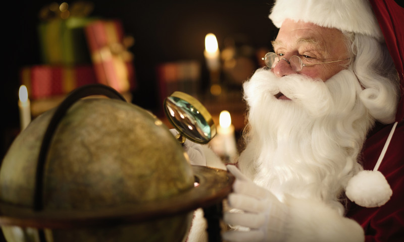 Santa Claus looking through magnifying glass at globe