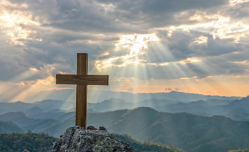 Silhouettes of crucifix symbol on top mountain with bright sunbeam on the colorful sky background