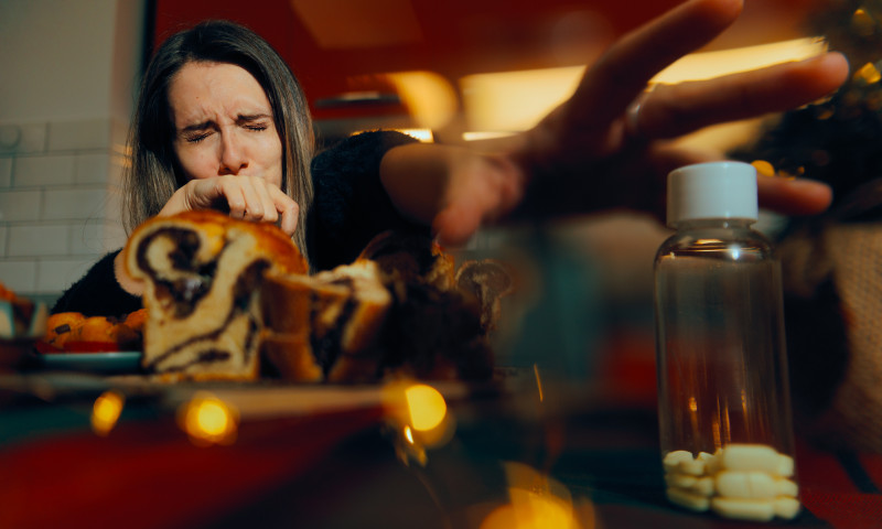 Woman Overeating on Christmas reaching for Stomachache Pills