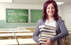 Portrait Of Cheerful Teacher Holding Stacked Books In Classroom