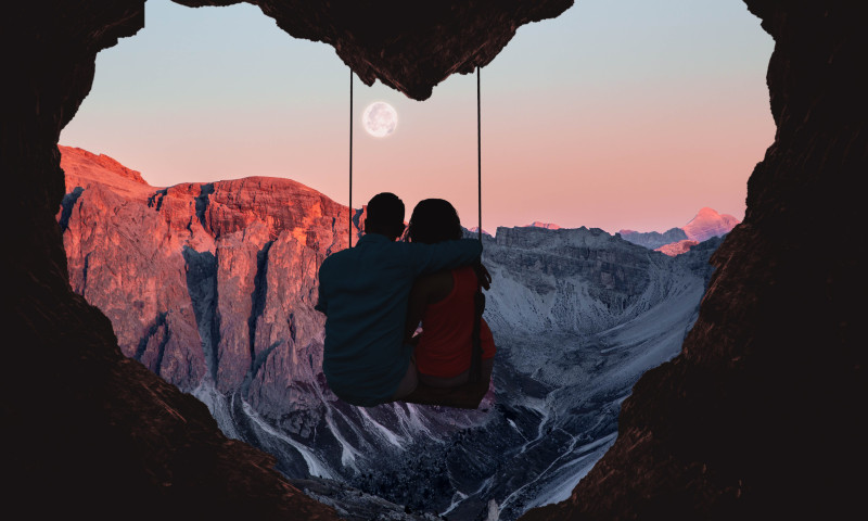 Couple on swing contemplating the mountains in a romantic view with heart shape.
