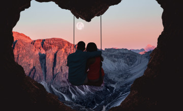 Couple on swing contemplating the mountains in a romantic view with heart shape.